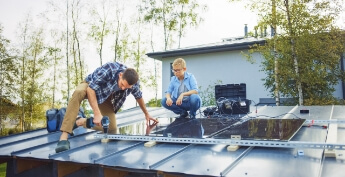 DIY weekend warrior man on house roof installing solar panels while young man watches nearby