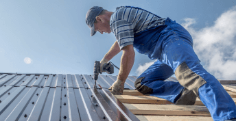 Roofing contractor instsalling metal roof panels holding a screw gun
