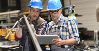 two engineers wearing blue hard hats looking at a piece of steel